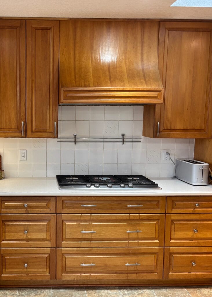 BEFORE UPDATE Kitchen with aged or darkened cherry wood abinets, laminate countertop, painted backsplash tile