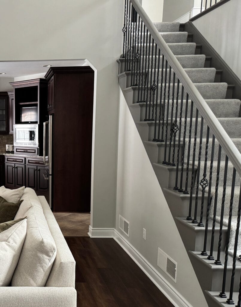 Benjamin Moore London Fog, greige taupe warm gray paint color on walls, painted Urbane Bronze railing, black iron, dark wood floor, carpet on stairs gray