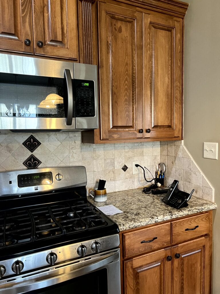 Dark stained pine wood cabinets, santa cecilia granite countertop, travertine tile backsplash, 2000s tuscan style kitchen