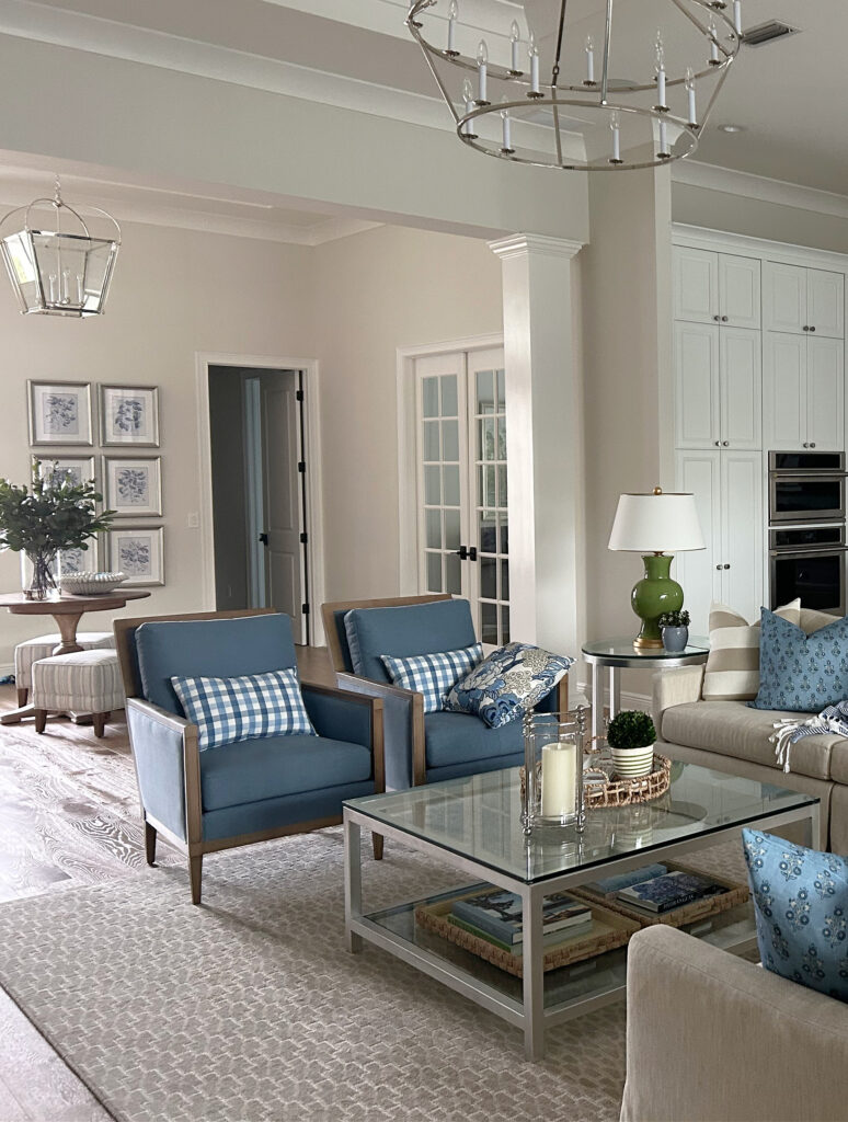 PPG Paraffin warm neutral paint color on walls, Delicate White trim, blue accent chairs, neutral rug, home decor, transitional style, high ceiling, chandelier