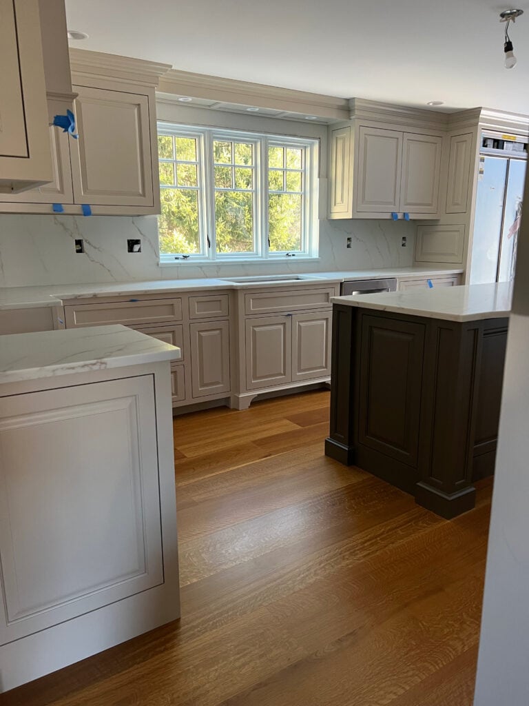 Sherwin Williams Accessible Beige painted kitchen cabinets, orange stain wood floor, dark island, warm white quartz countertop and slab backsplash