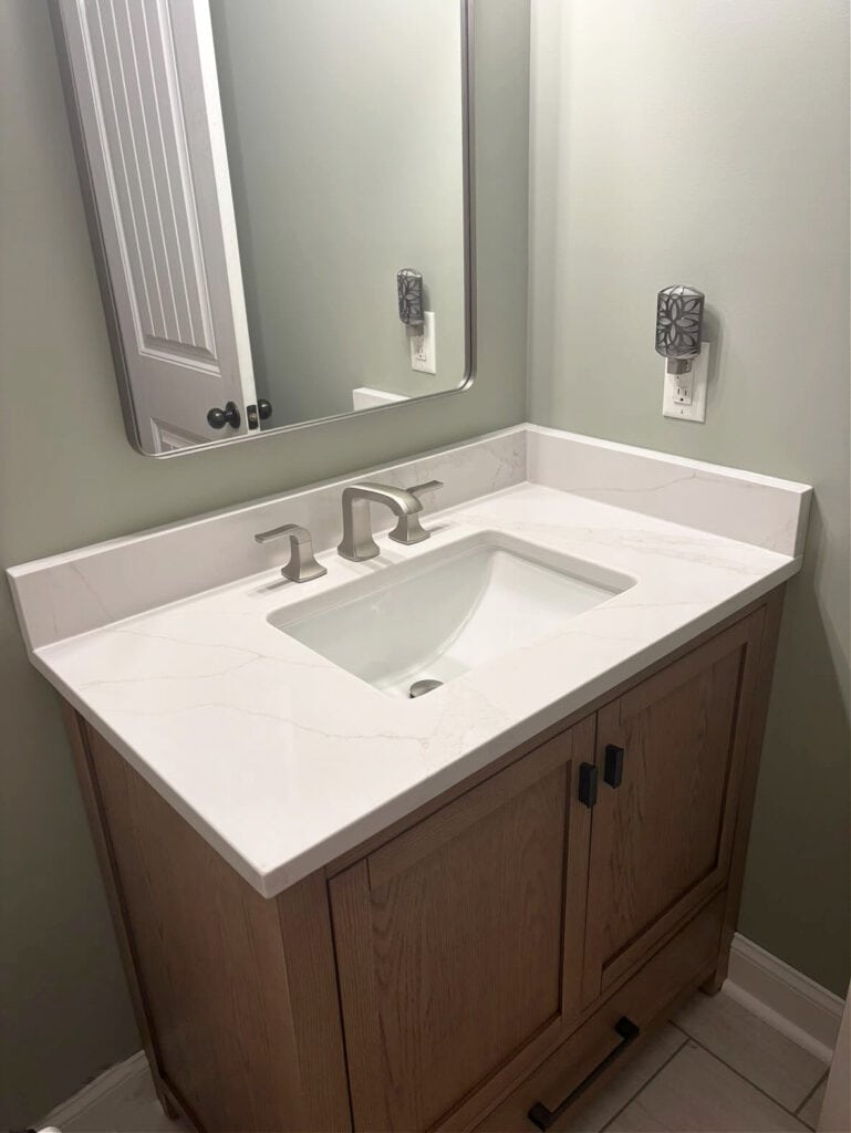 Sherwin Williams Comfort Gray, green-gray paint color in small bathroom with white quartz countertop, oak wood vanity