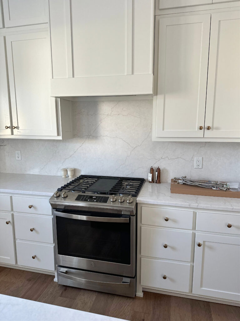 Sherwin Williams Pure White cabinets in kitchen with off-white warm gray quartz countertop with beige brown veins, range hood cabinet, stainless steel appliances