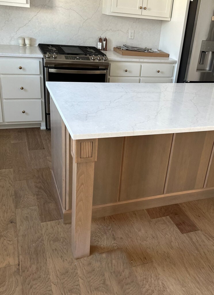 off-white warm gray quartz countertop on island with wood, wood flooring, Sherwin Williams PUre White kitchen cabinets, gold hardware