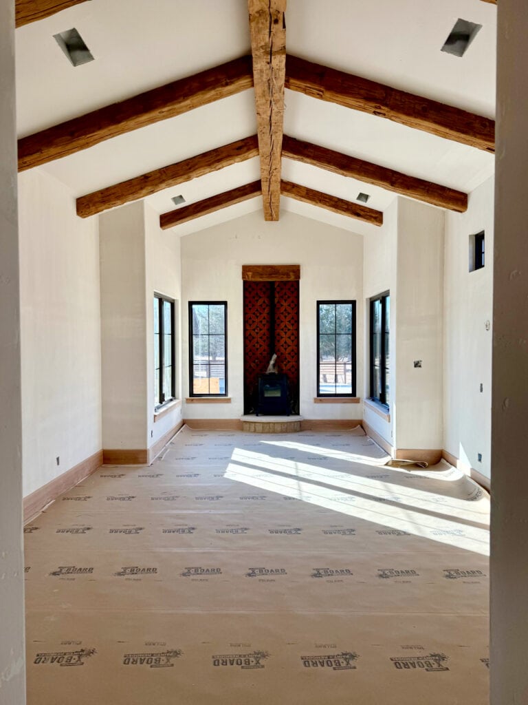 primary bedroom with wood beams and red orange tile around fireplace, black windows, warm white walls