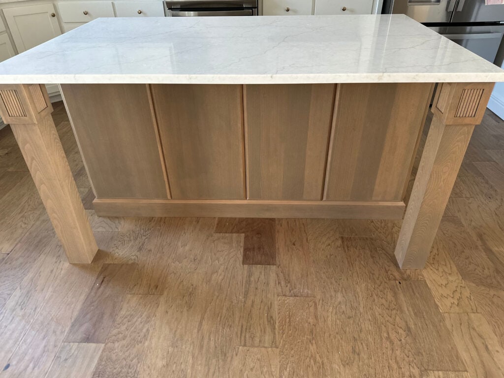 wood island with wood flooring, off-white warm gray quartz countertop with white cabinets in kitchen