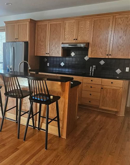 wood trim, golden oak wood cabinets and floor, raised kitchen island with black granite or corian countertops, stainless steel appliances