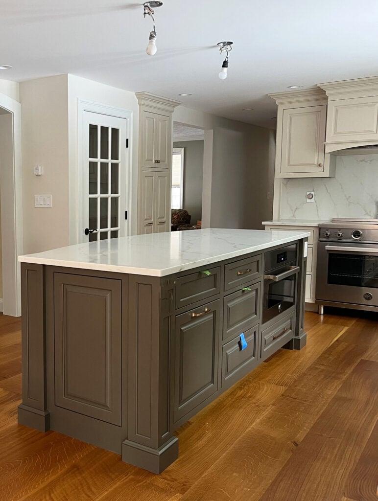 Island painted Sherwin Williams Urbane Bronze, dark greige, warm white quartz countertop, gold veins, Accessible Beige kitchen cabinets, slab backsplash, wood floor