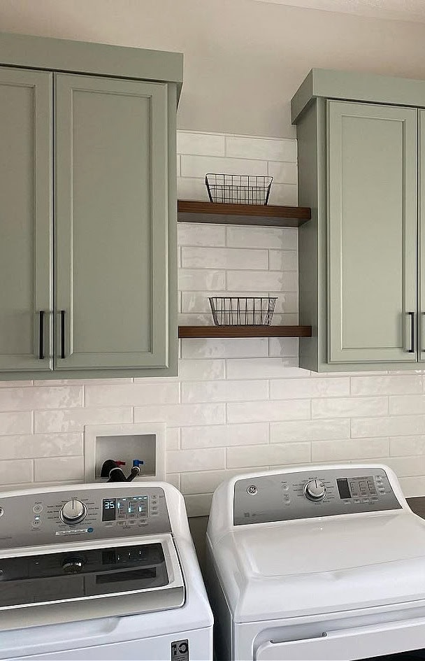 Laundry room painted cabinets similar to Sherwin Williams Evergreen Fog, green, subway tile backsplash, white washer and dryer, floating shelves