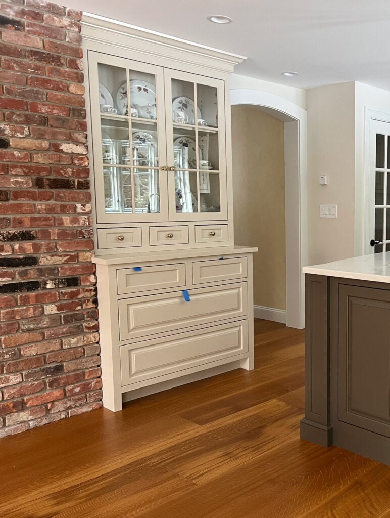 Sherwin Williams Accessible Beige painted kitchen cabinets, wood floor, urbane Bronze island, AEsthetic White walls, brick accent wall