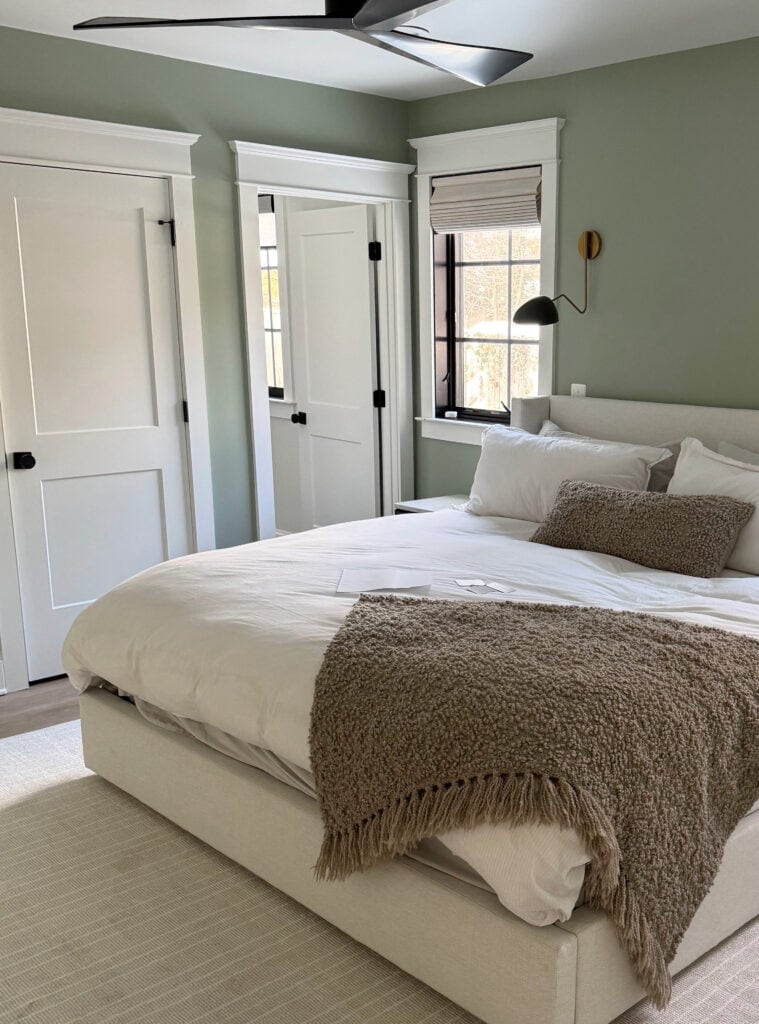 Sherwin Williams Cascade Green, best green paint color, with linen colored fabric headboard, striped area rug, bed linens, wall mount light sconce, bedroom