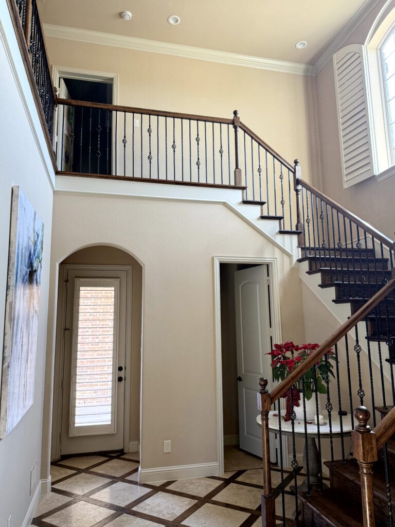 Similar to Sherwin Williams Kilim Beige, warm off-white almost cream trim, checkerboard trellis travertine and dark wood floor, staircase with wood railing