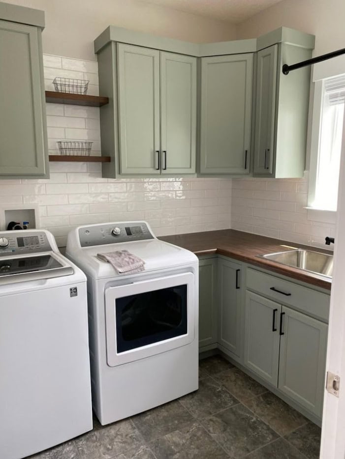 painted wood laundry room cabinets, linoleum vinyl floor, butcher block countertop, white washer and dryer, similar to Sherwin Williams Evergreen Fog green cabinets, subway tile