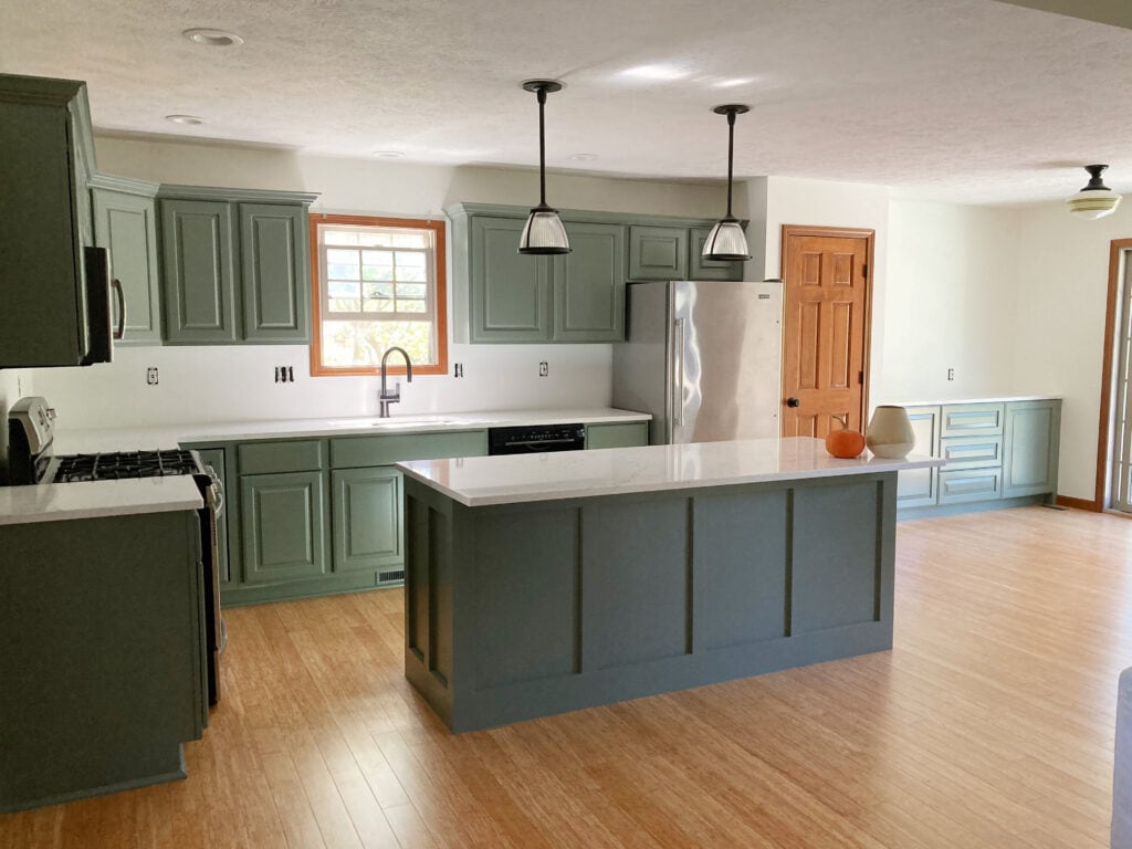 Green painted wood kitchen cabinets, Benjamin Moore Chantily Lace white walls, Sherwin Williams Retreat, wood floor, island, white quartz countertop, wood trims