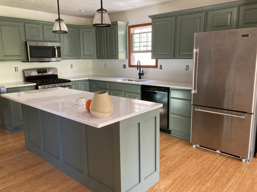 Benjamin Moore Chantilly Lace white walls, Sherwin Williams Retreat painted green wood kitchen cabinets, wood floor, white quartz countertop, wood trim