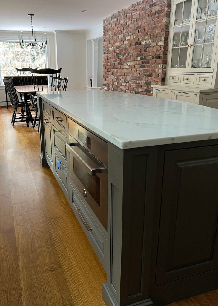 Wood flooring, painted kitchen cabinets Accessible Beige, island is painted Sherwin williams Porpoise, brick accent wall