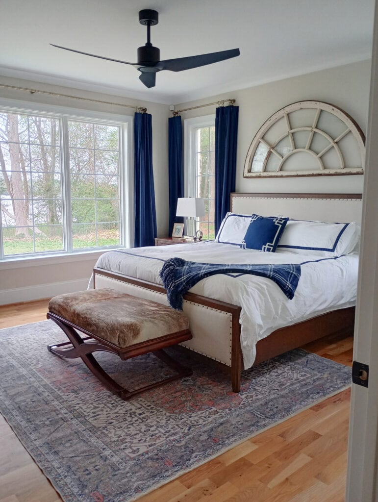 Benjamin Moore Winds Breath in primary bedroom, Pure White trim, crown molding, navy blue accents, drapes, wood floor, upholstered headboarsd and bed frame