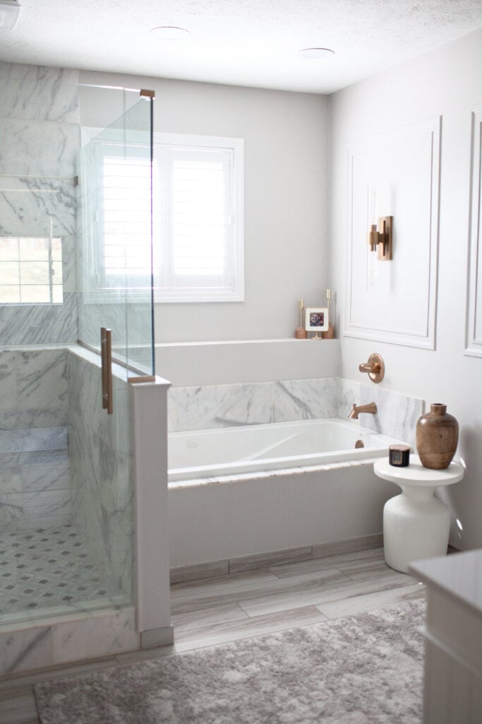 Ensuite bathroom, bathtub, walk in shower, marble floor, marble walls, wood-look tile floor, Sherwin Williams ON the Rocks gray walls, copper finish faucet and wall light sconce, white trim