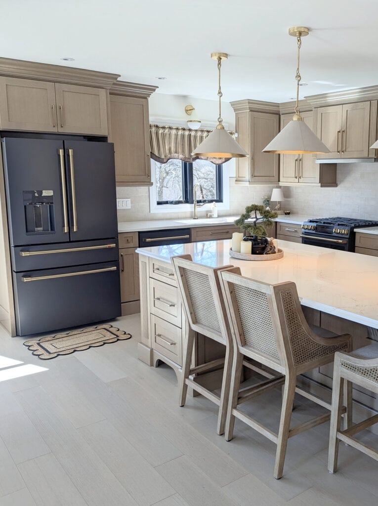 GE Matte black fridge appliances, brushed brass hardware, staineed oak beige-wash wood floor, white quartz island, Vicostone, Misterio Gold, wood rattan stools, white pendants, Zellige backsplash tile