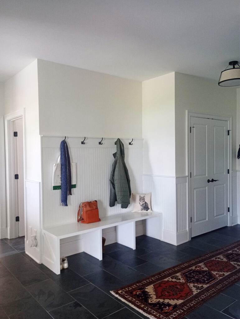 Mudroom with builtin bench, beadboard, wall hoooks, Sherwin Williams Pure White trim, Alabaster warm white walls, dark gray black slate tile floor