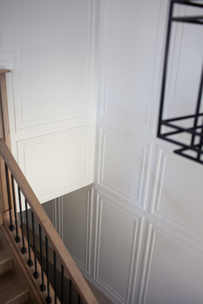 Staircase in split level home entryway. Wainscoting, trims and moldings added to walls painted Sherwin Williams Cold Foam, wood hand railing, black spindles.