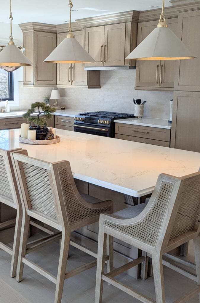 Wood and woven rattan counter stools, white quartz countertop, Vicostone Misterio Gold, custom stained wood cabinets, zellige backsplash, gold hardware, white pendant lights