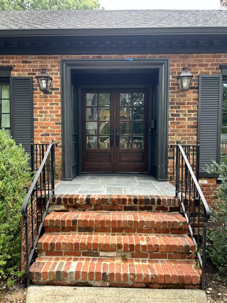 exterior with red, orange and brown brick, dark soft black painted trim, shutters, and dentil molding, double front doors in wood stain.