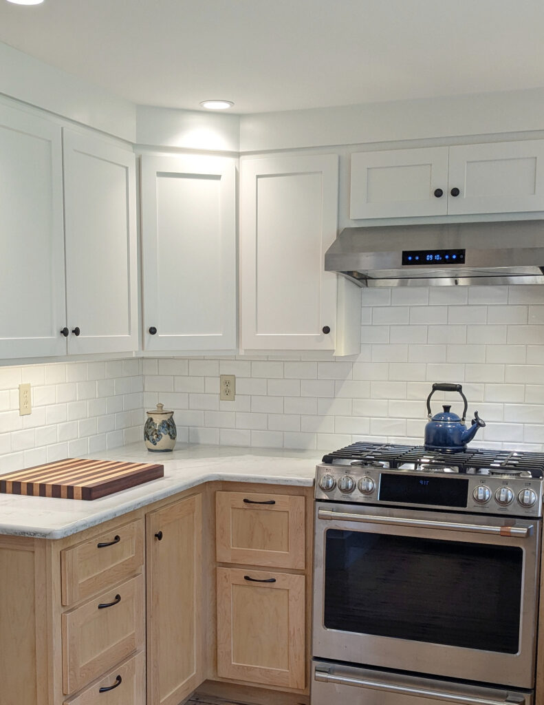 Sherwin Williams Alabaster painted warm white cabinets, subway tile backsplash, maple wood lower cabinets, stainless steel countertop. Emerstone Dynamic Gold white quartz countertop