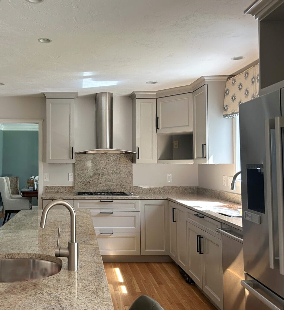 Benjamin MOore Plymouth Rock, Valley Forge Tan, painted maple wood kitchen cabinets, granite countertop and slab backsplash behind stove, black hardware, Windfresh White taupe walls.