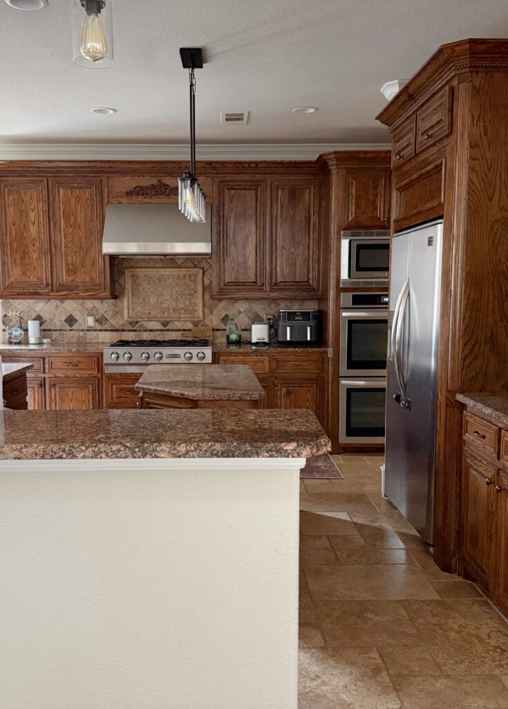 Dark oak stained wood kitchen cabinets, outdated baltic brown look granite countertop, travertine tile backsplash and flooring, dark kitchen, large island