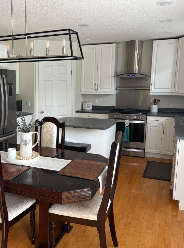 Kitchen after painting alder wood cabinets, maple floor, Benjamin Moore White Down and Simply White, black laminate countertop, stainless steel appliances, dark cherry red dining room wood set