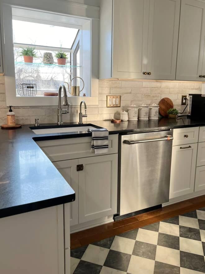 Sherwin Williams Pure White painted kitchen cabinets, black honed granite countertop, black and white checkered floor mat, brass hardware, tile backsplash