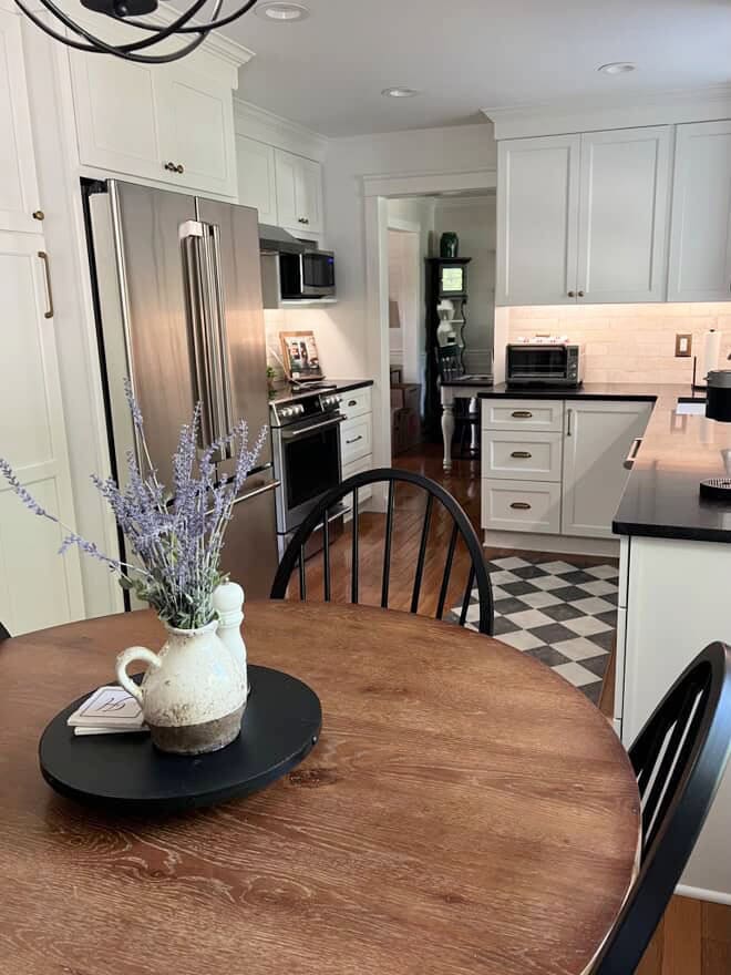 Sherwin Williams Pure White painted kitchen cabinets, oak floor and table, brass hardware, black honed granite countertop, 1990s or 2000s kitchen update