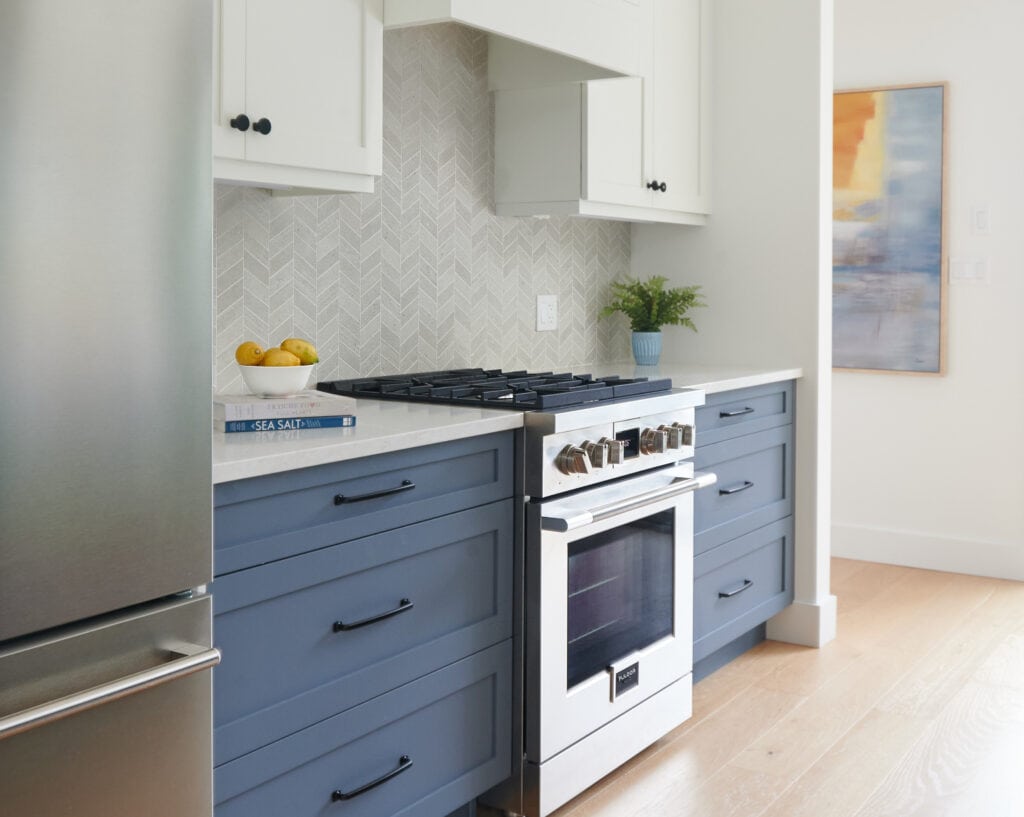 Kitchen, Benjamin Moore White Dove, warm white cabinets and paint on walls, Brittania Blue lower cabinets, island, stainless steel, Fulgor, chevron backsplash, Omnia quartz, white oak floor