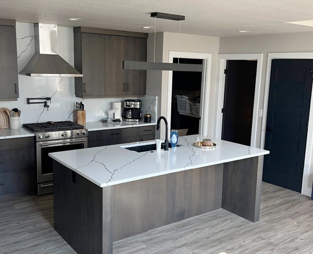 Tricorn Black interior doors, STAINLESS APPLIANCES, BLACK HARDWARE, Sherwin Williams Alpaca with wood island, dark wood cabinets, gray wash flooring, white quartz veins