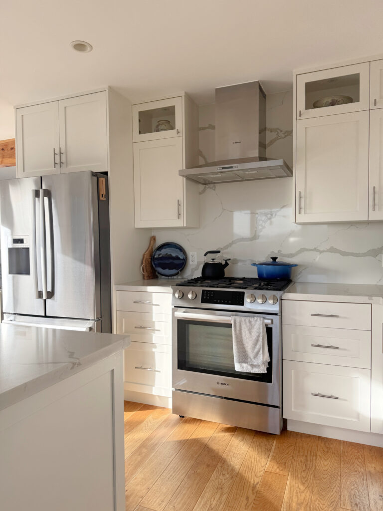 Benjamin Moore Cloud White painted cabinets with white quartz and original fir flooring, slab backsplash and wall mount chimney range hood