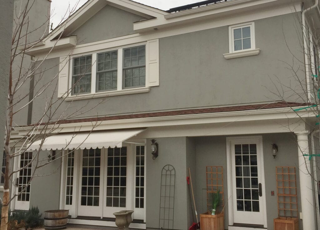 Benjamin Moore Rockport Gray painted exterior stucco on cloudy day. Shutters, trims and gutters are creamy white Sail Cloth.