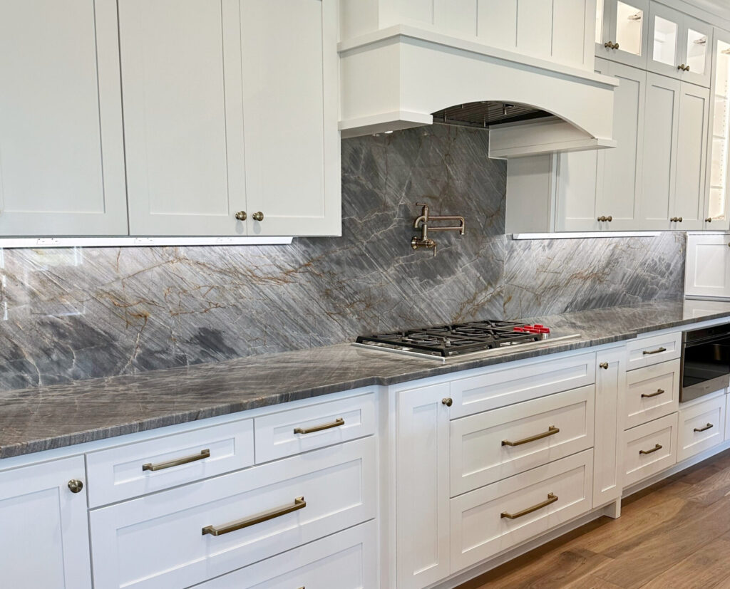 Dark Gray blue quartzite countertops, wood walnut look flooring, Sherwin Williams Pure White cabinets, glass doors on top, pot filler