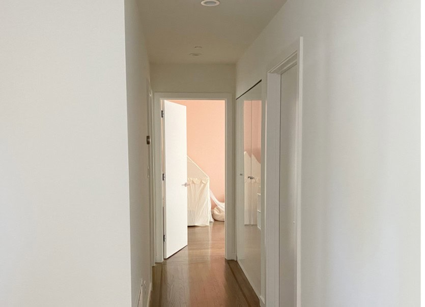 Kelly Moore Swiss Coffee warm white paint color with medium stained oak flooring down darker hallway, pink bedroom at end