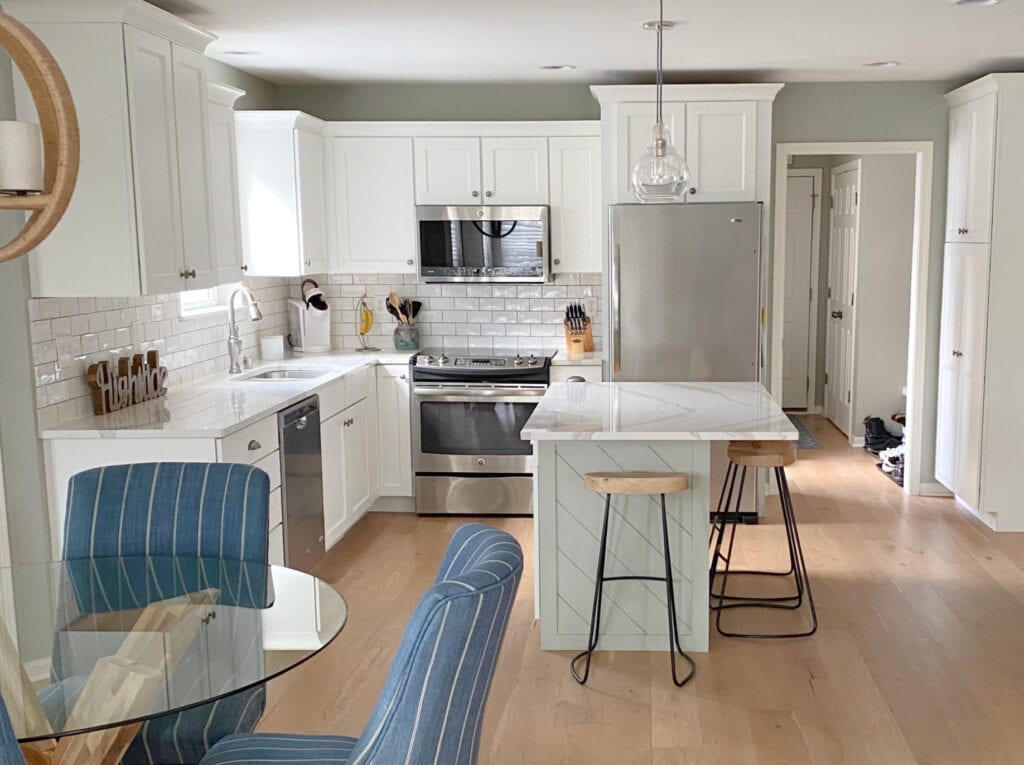 Sherwin Williams Pure White kitchen cabinets, Austere Gray (gray-green) painted island, and walls, natural red oak flooring, blue accents, white subway tile with dark grout