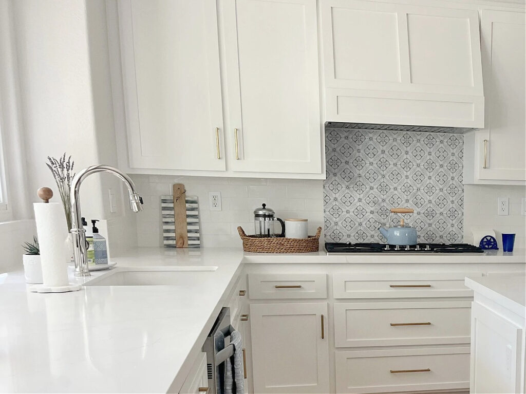 Sherwin Williams Pure White cabinets, subway tile backsplash with blue tile insert above stove, gold hardware, Classic Gray on the walls