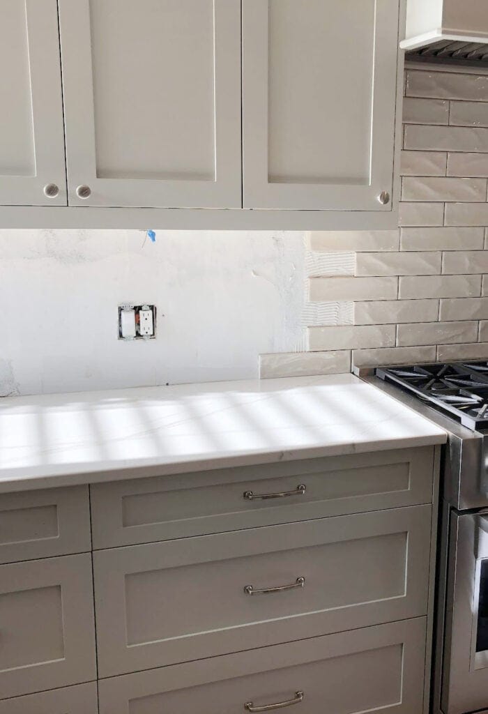 Benjamin Moore Revere Pewter darkened on painted kitchen cabinets, greige subway tile backsplash, Cambria Brittanica Warm off-white quartz countertop