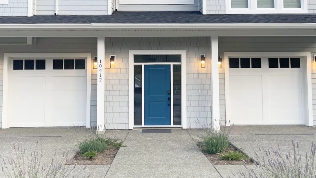 Sherwin Williams white trim, gutters, windows, and matching garage doors, Connor's Lakefront blue front door, James Hardie LIght Mist shakes and dark gray-black roof copy