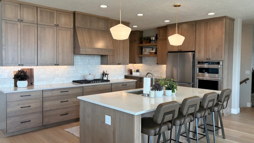 Stained wood kitchen cabinets, wood floor and island. White quartz countertop and zellige look subway tile backsplash with gold pendant lights (2)