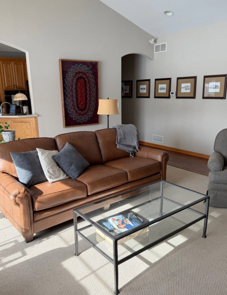 Revere Pewter with beige carpet, wood trim, brown leather sofa and a vaulted ceiling